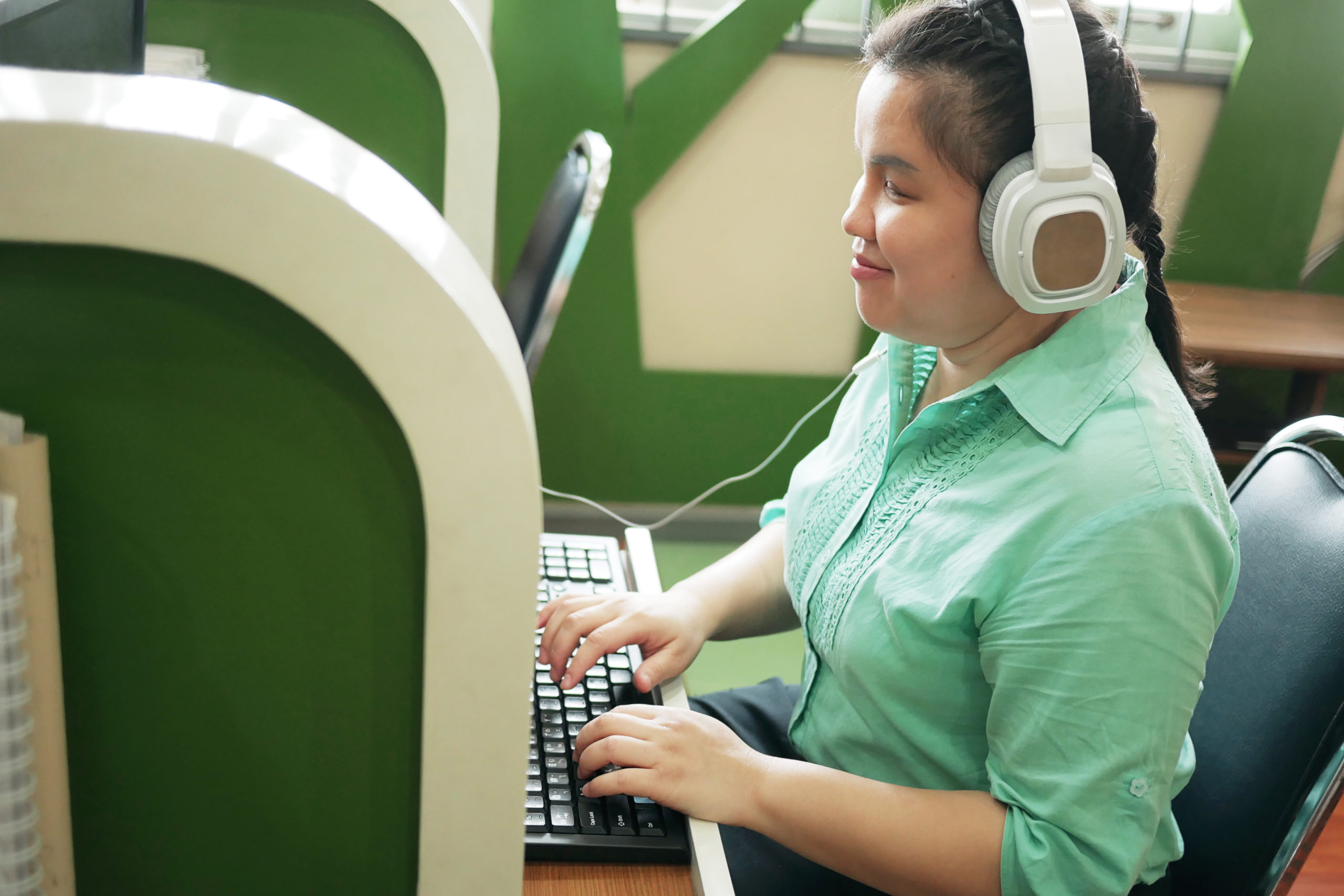 a blind girl using headphones on the computer in a library