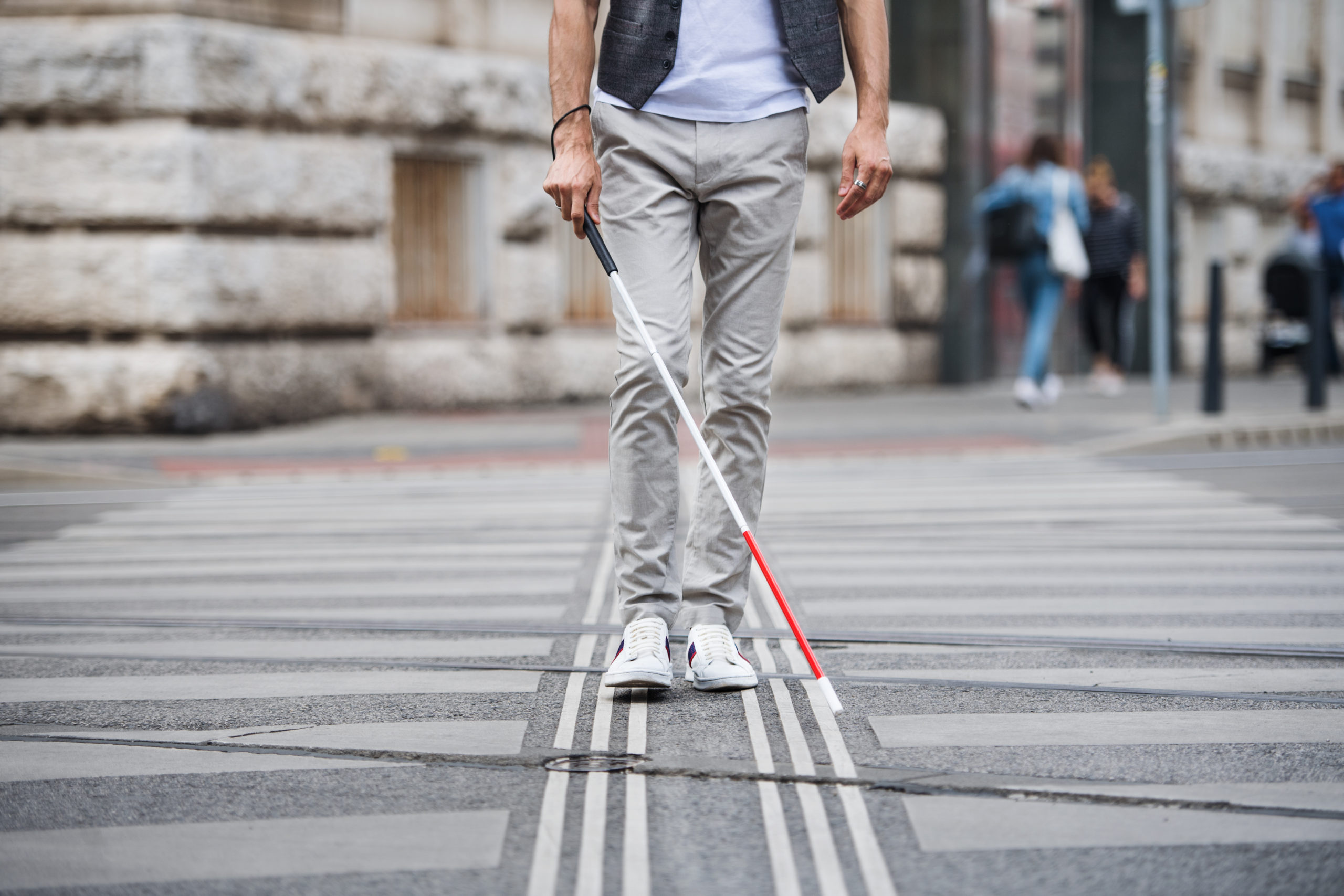 a man using a white tip cane walking across the street
