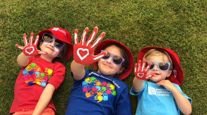 Happy children laying on grass showing their hands with hearts painted on their palms