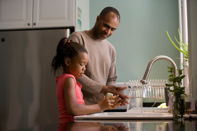 Father standing next to his young daughter at the kitchen sink, teaching her to wash her hands