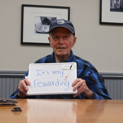 Volunteer, Cliff Smith holds a white board saying he likes to volunteer because it's rewarding