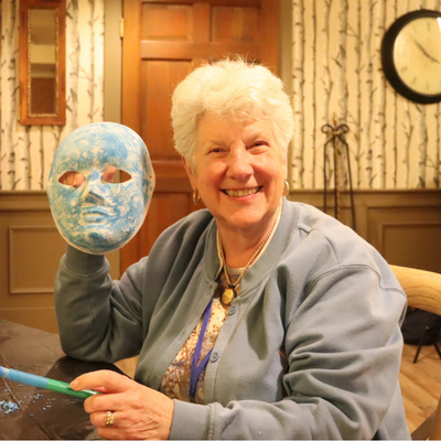a Silver Retreat participant smiles at the camera, holding up a mask they painted