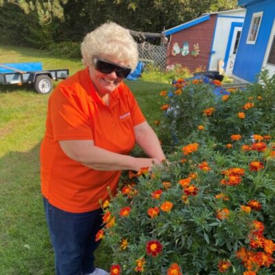 A senior woman wearing UV filtered glasses tends the orange flowers in her garden.