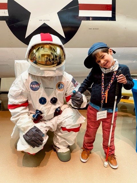Manny stands with his white cane next to an Astronaut figure
