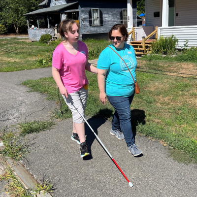 staff helping a teen walk with a white cane