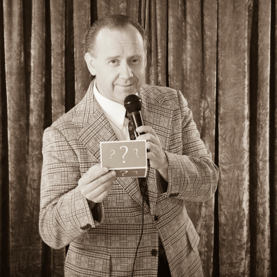 a game show host holds out a piece of paper with question marks on it