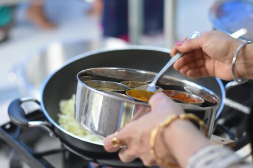 A pair of hands spooning ingredients into a pot.