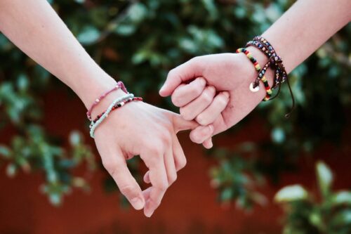 Two friends wearing bracelets hold hands.