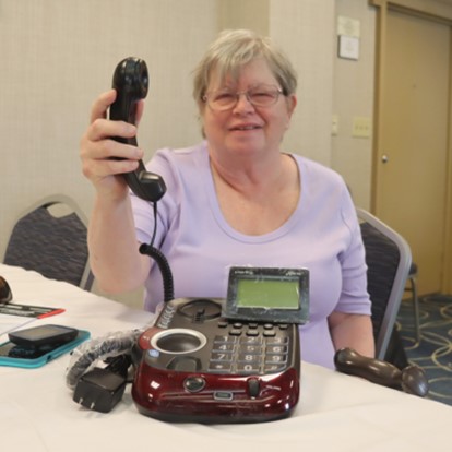 A senior woman holds up the receiver of a Clarity AltoPlus phone. The large buttons on the machine are visible.