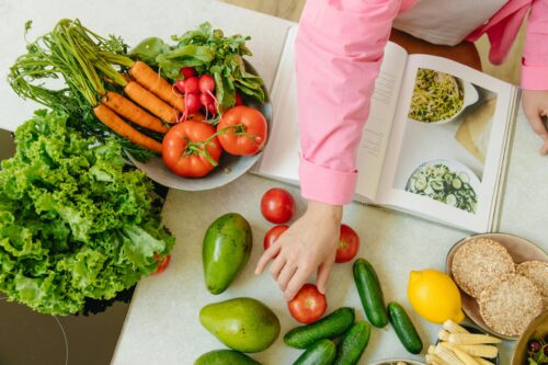 A counter with vegetables and other ingredients and an open cookbook on it.