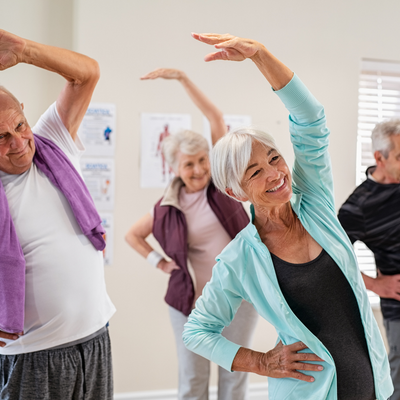 A group of seniors dressed in workout clothes do a stretch.