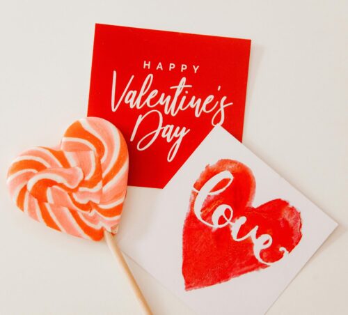 A heart shaped lollipop with two Valentine's day cards beside it.