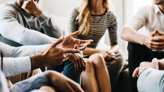 A group of people sitting in a circle listen as one person talks.