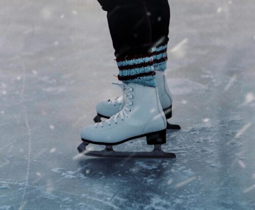 A pair of feet in ice skates on the ice, with cozy socks peeking out of the skates.