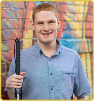 Christopher Duffley holding a white cane in front of a colorful wall.