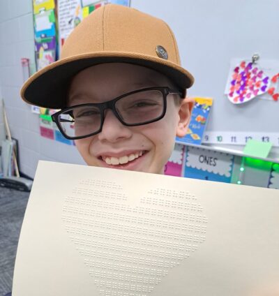 A boy holds up a heart he designed using braille.