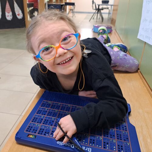 A young girl wearing glasses excitedly works on a braille activity.