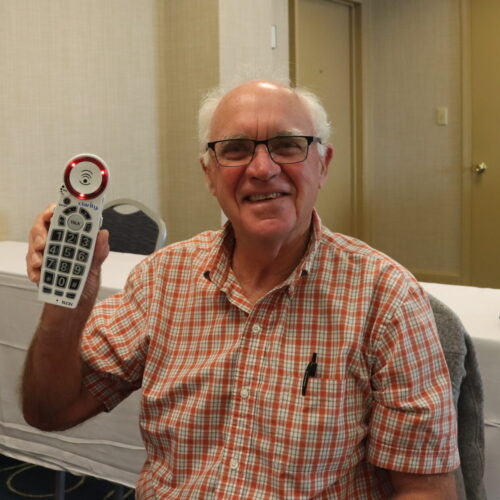 A senior man holds up a TEAP cordless phone with large buttons that light up.