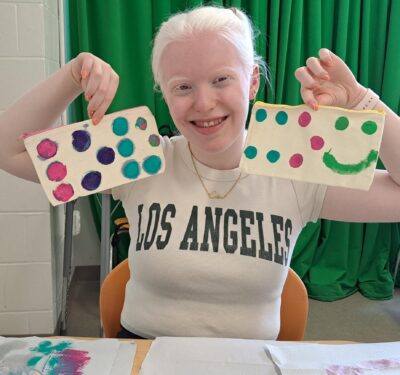 A teen girl holding up a craft with colorful painted braille.