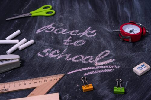 The words Back To School written on a chalk board with school supplies on it, like erasers, binder clips, and scissors.