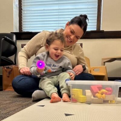 A woman with a baby boy on her lap playing with a brightly colored ball.