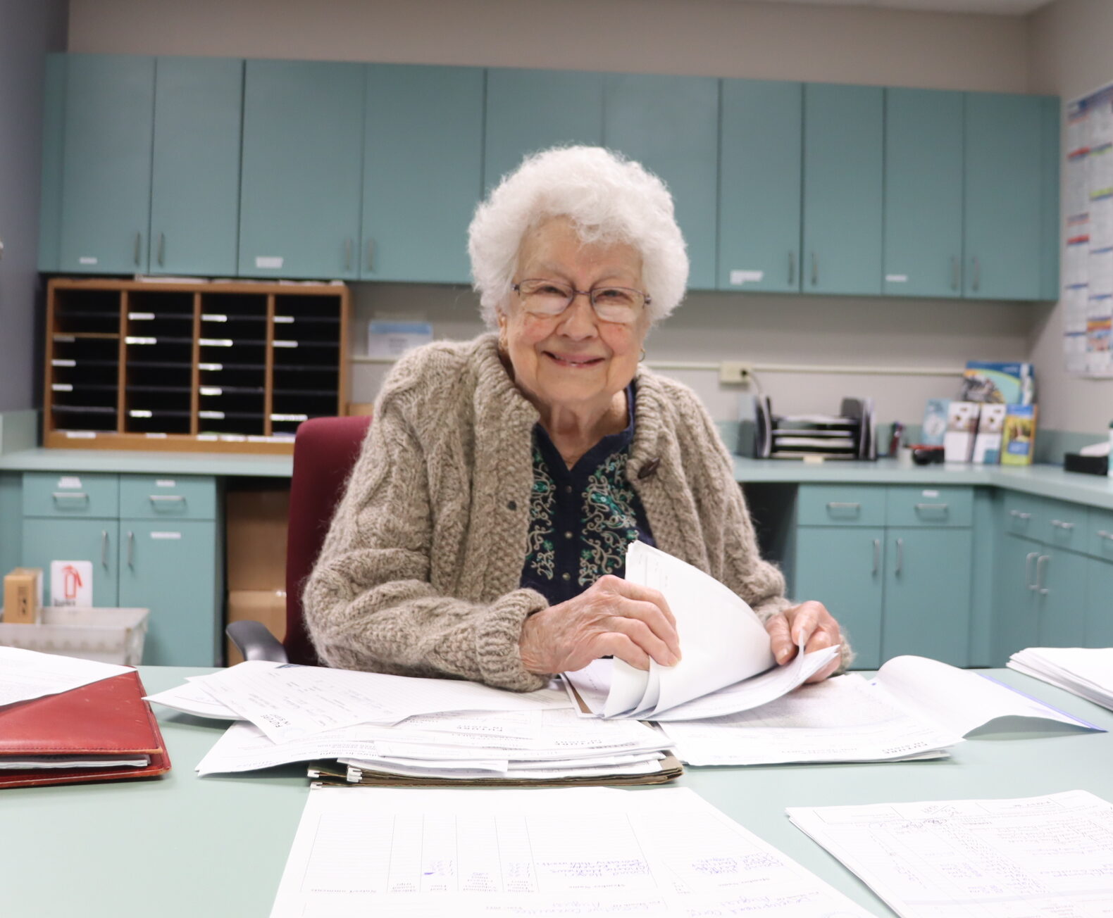 A senior woman flips through paperwork at the front desk of the Future In Sight office.