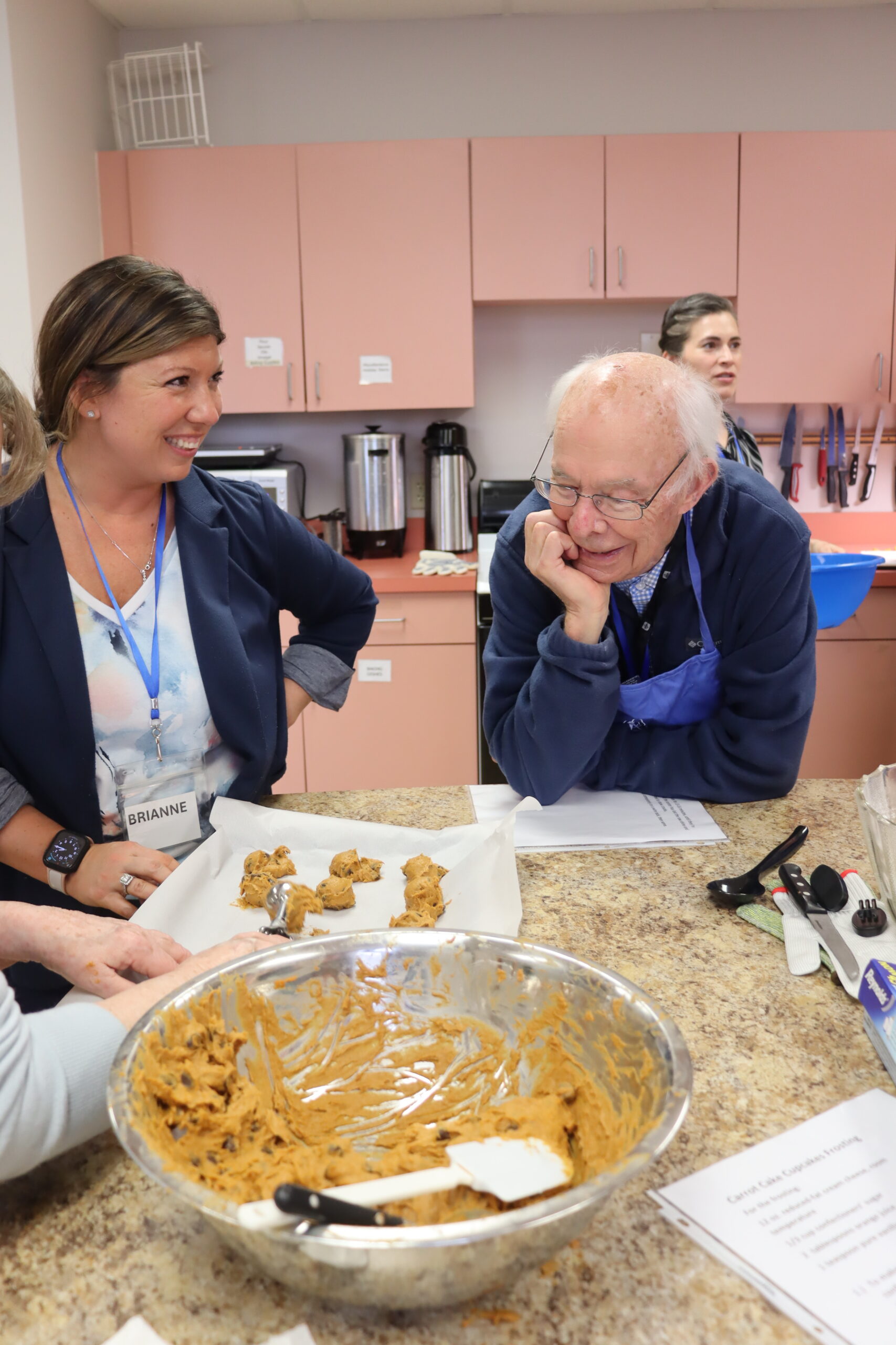 A female instructor and a senior man scoop cookie dough onto a tray.