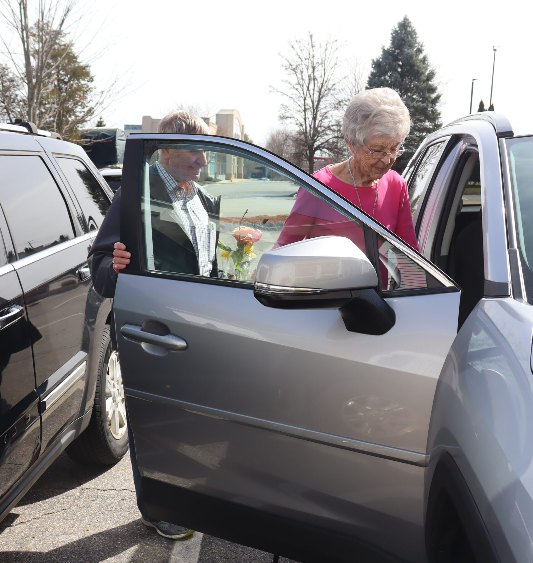 A middle aged man holds the door of a car as a senior woman enters.