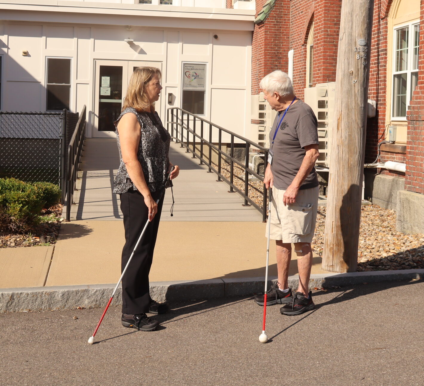 A female orientation & mobility specialist teaches a man with a white cane on a sidewalk.