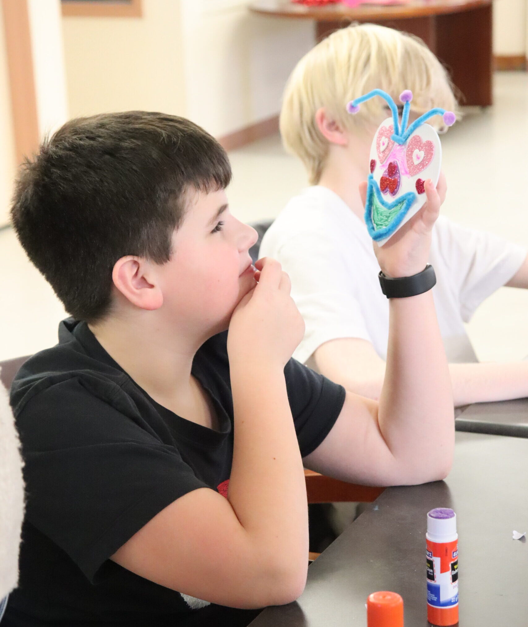 A boy looks proudly at the heart craft he has made.
