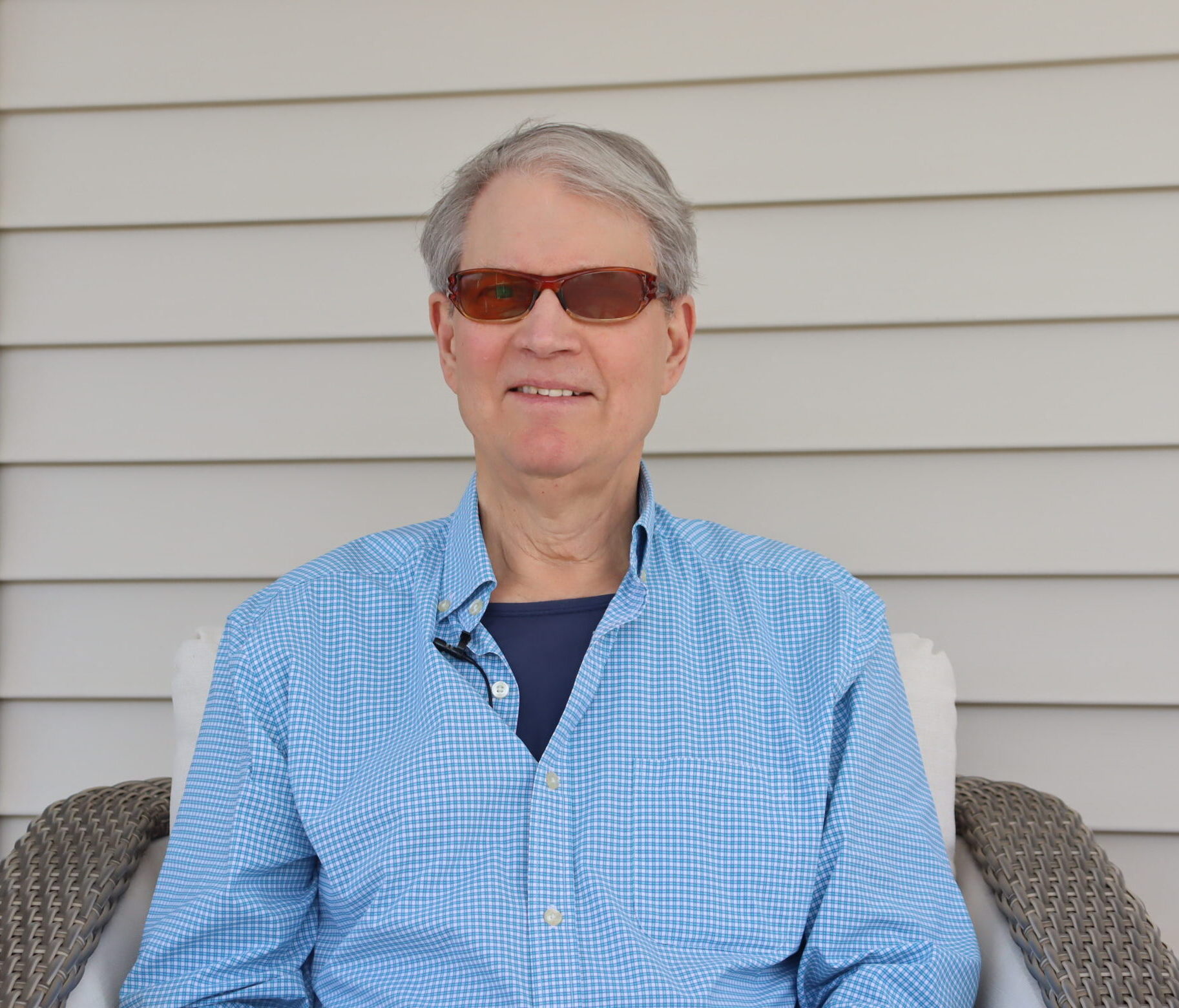 A man in dark glasses sits outside with a smile.