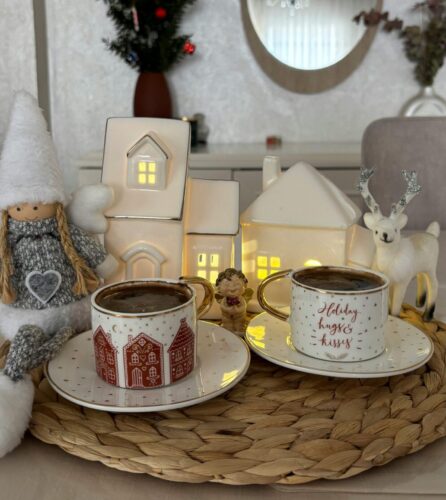 Two mugs of hot cocoa surrounded by white, winter-themed decorations.