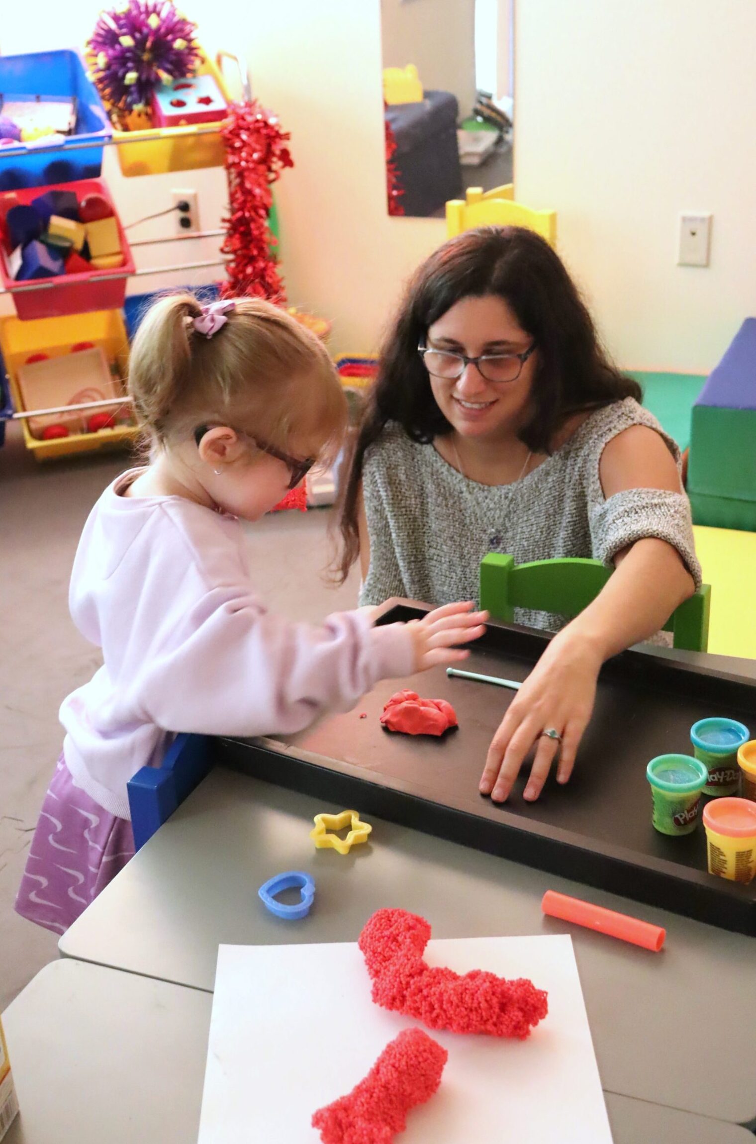 A female teacher plays with Play-Doh with a young girl.
