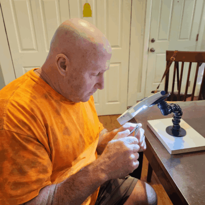 A senior man uses a magnifier with a light to clip his fingernails.