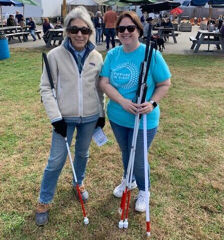 A woman with a white cane stands and smiles with a Future In Sight staff member holding several white canes.