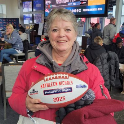 Kathy Nichols holding up a football with her name and Future In Sight on it.