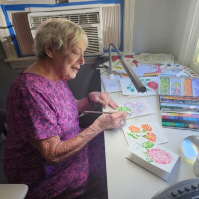 A senior woman watercolor paints by lamplight.