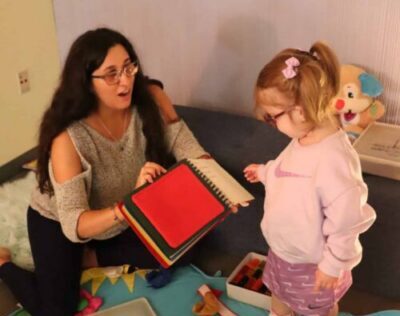 A woman with Future In Sight reads a book to a little girl on a playmat.
