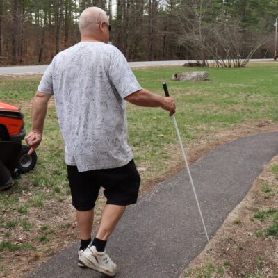 A man uses a white cane to navigate an outdoor walkway.