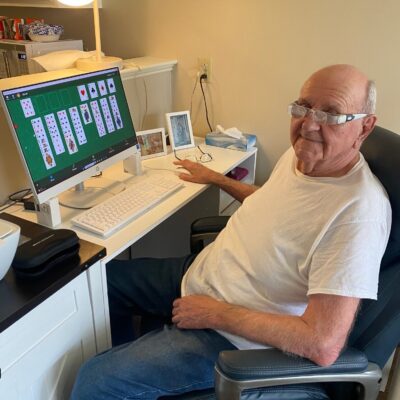 A senior using special glasses to play solitaire on a computer.