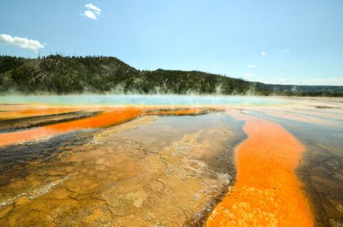 A dramatic landscape in Yellowstone Park with colorful water and trees in the distance.