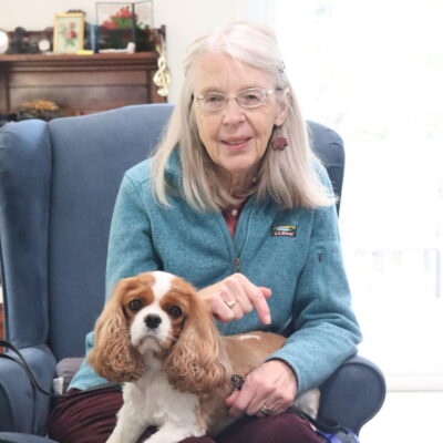 A senior wearing glasses with a dog on her lap.