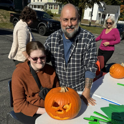 A teen and her parent posing with a jack-o-lantern.